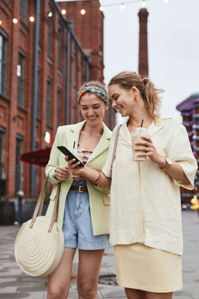 Two women in stylish outfits standing outside looking at a phone.
