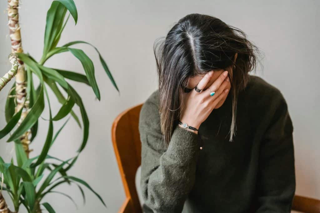 Women with dark hair wearing a dark green shirt sitting with her head down in her hands.