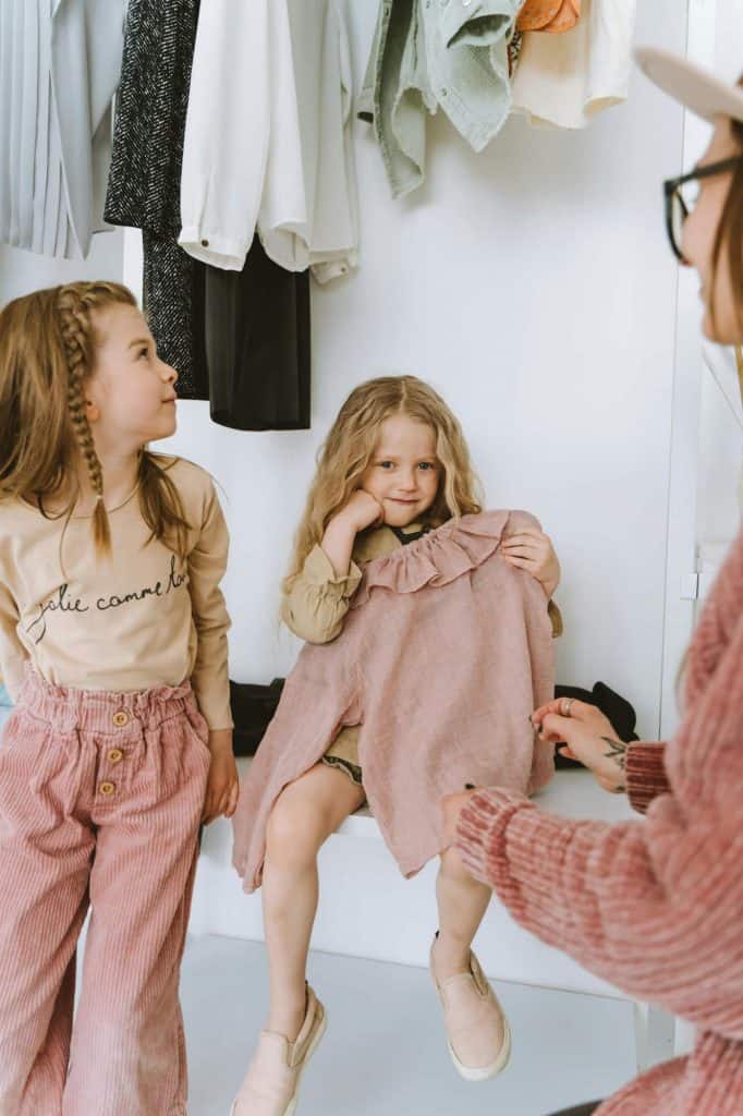 Mom and 2 daughters sitting in a closet while the girls look at clothes.
