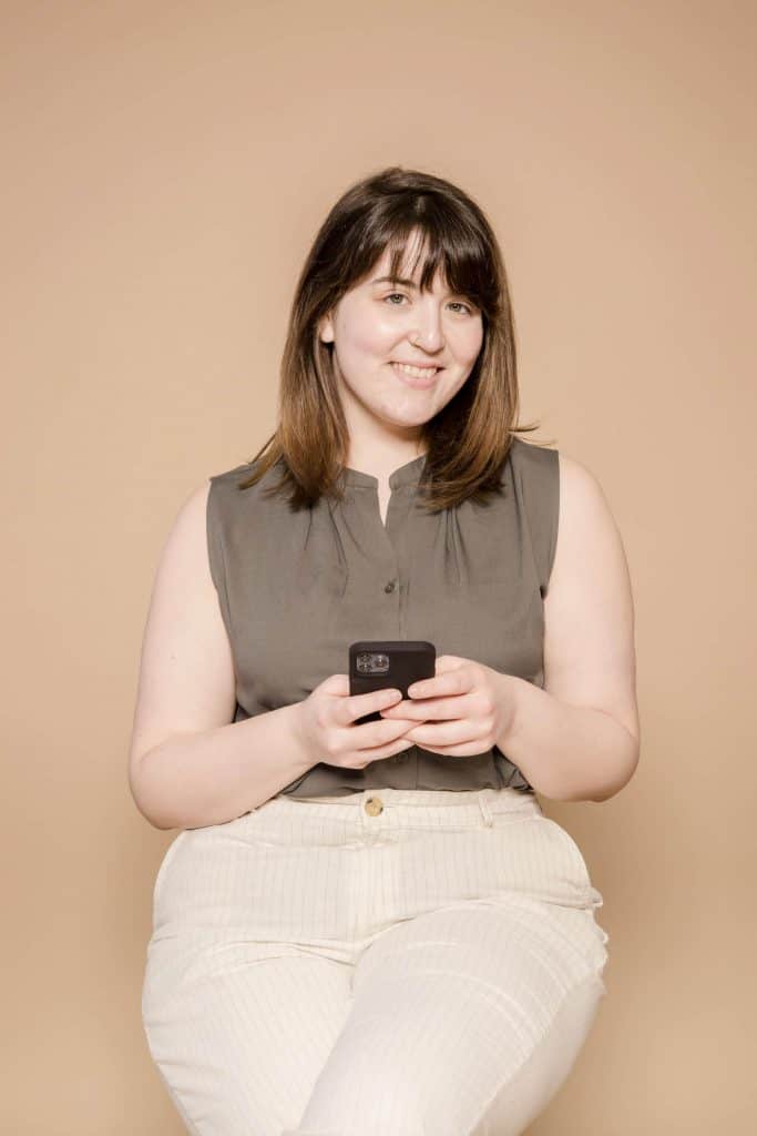 Woman with brown hair and bangs wearing a nice outfit while holding a phone.
