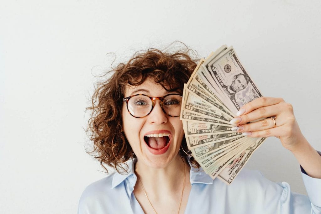 Woman with curly hair wearing glasses holding a bunch of money in her hand.