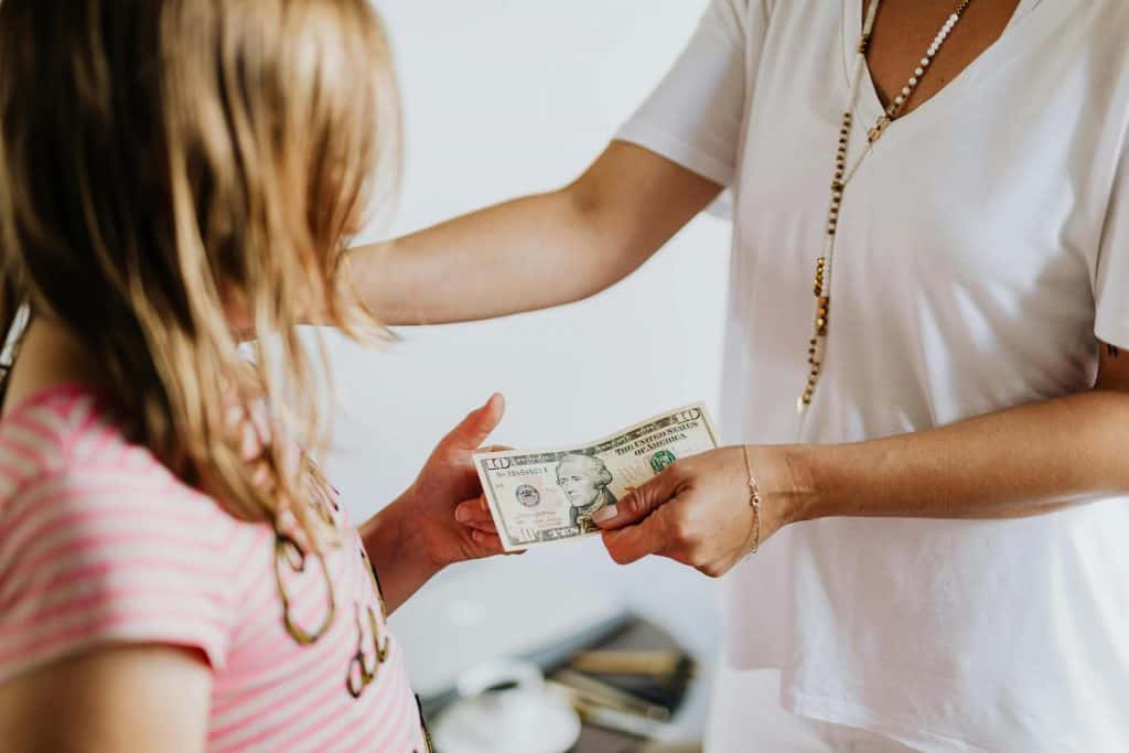 Woman handing a young girl a 10 dollar bill.