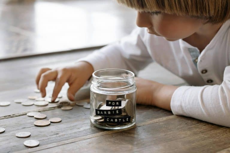 kid putting coins in a glass jar to save for a toy she wants