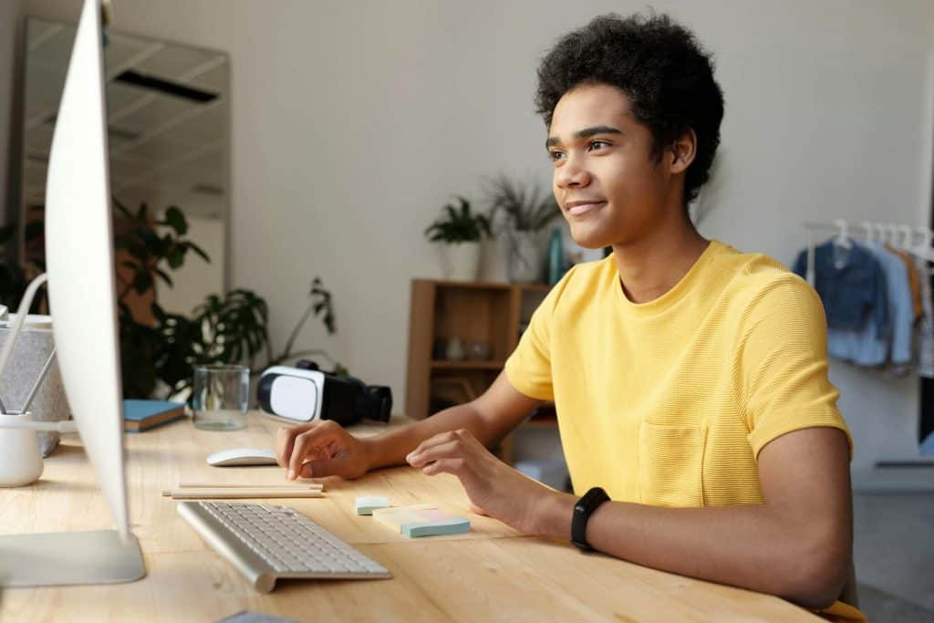 Teenage boy sitting at a computer in a yellow shirt learning about investing.