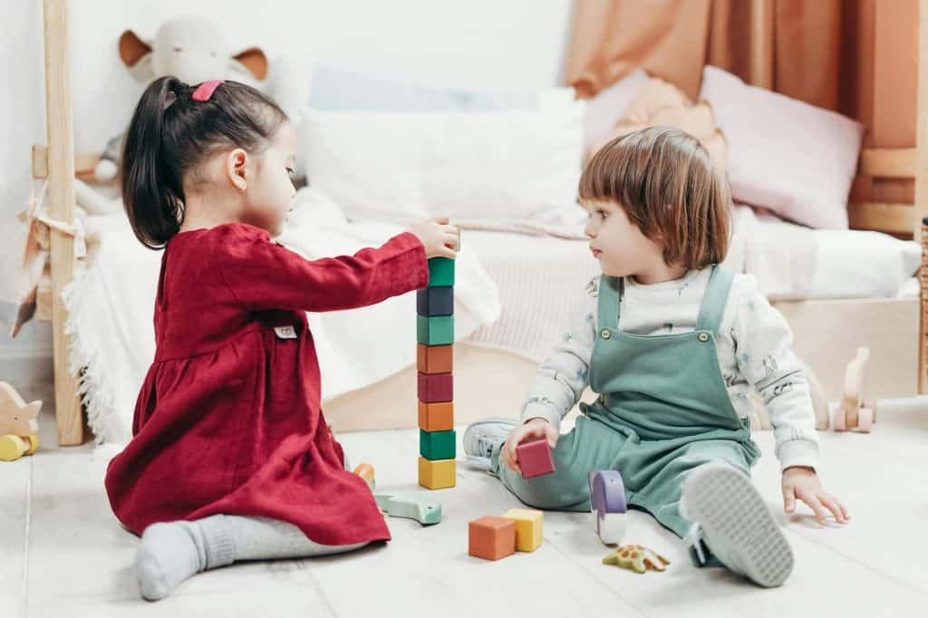Two toddlers sitting on the floor stacking blocks.
