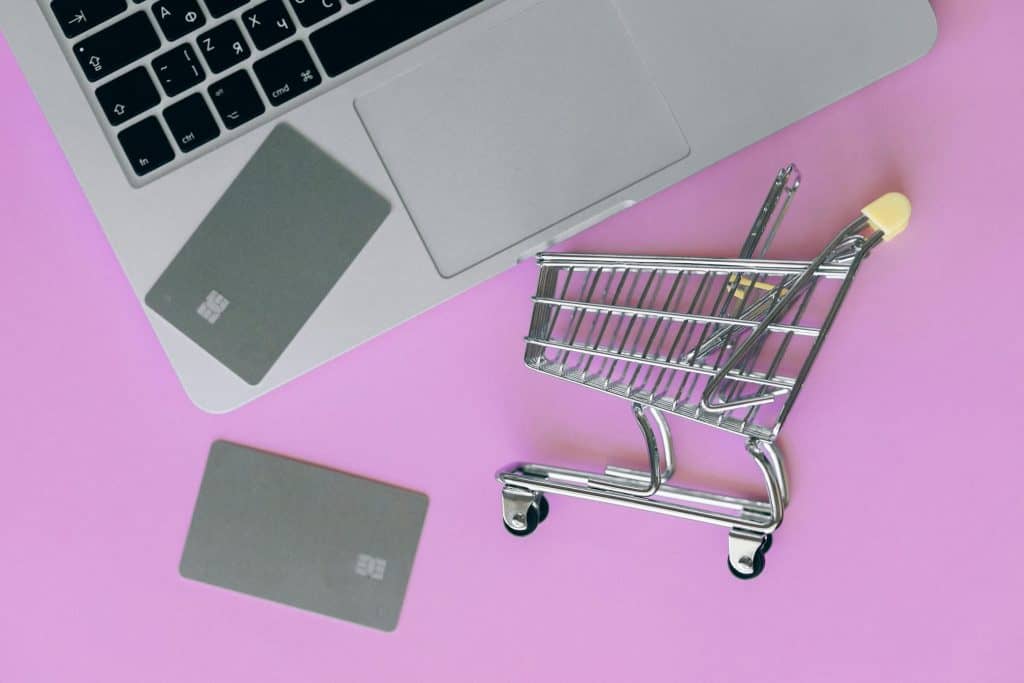 Image of a laptop with 2 credit cards sitting on it and a tiny toy shopping cart. 