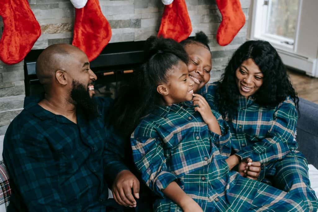 Family all sitting together smiling while wearing flannel Christmas pajamas. 