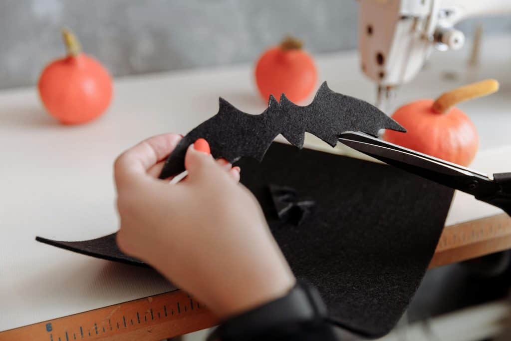 Image of hands cutting a bat out of black felt with small pumpkins in the background. 