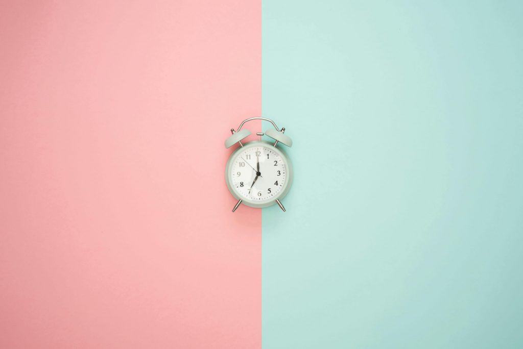 A analog clock with a pink and aqua background behind it. 