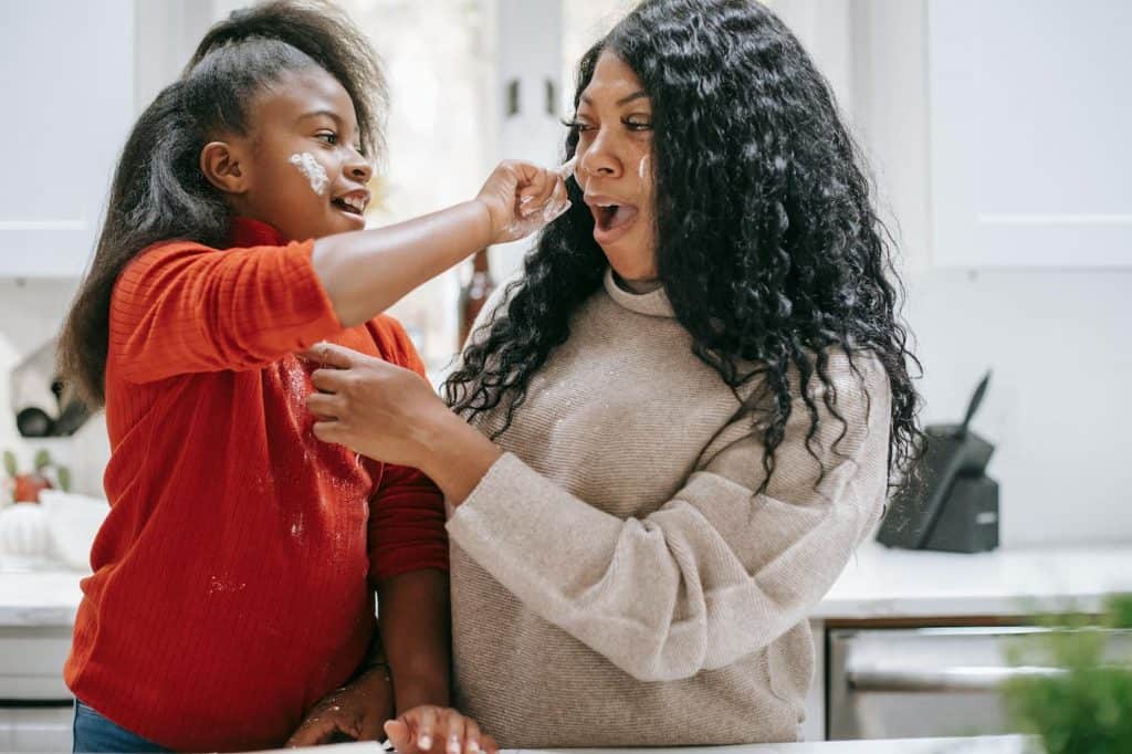 A girl and her mom in the kitchen having fun. They are wiping flour on each others faces. 