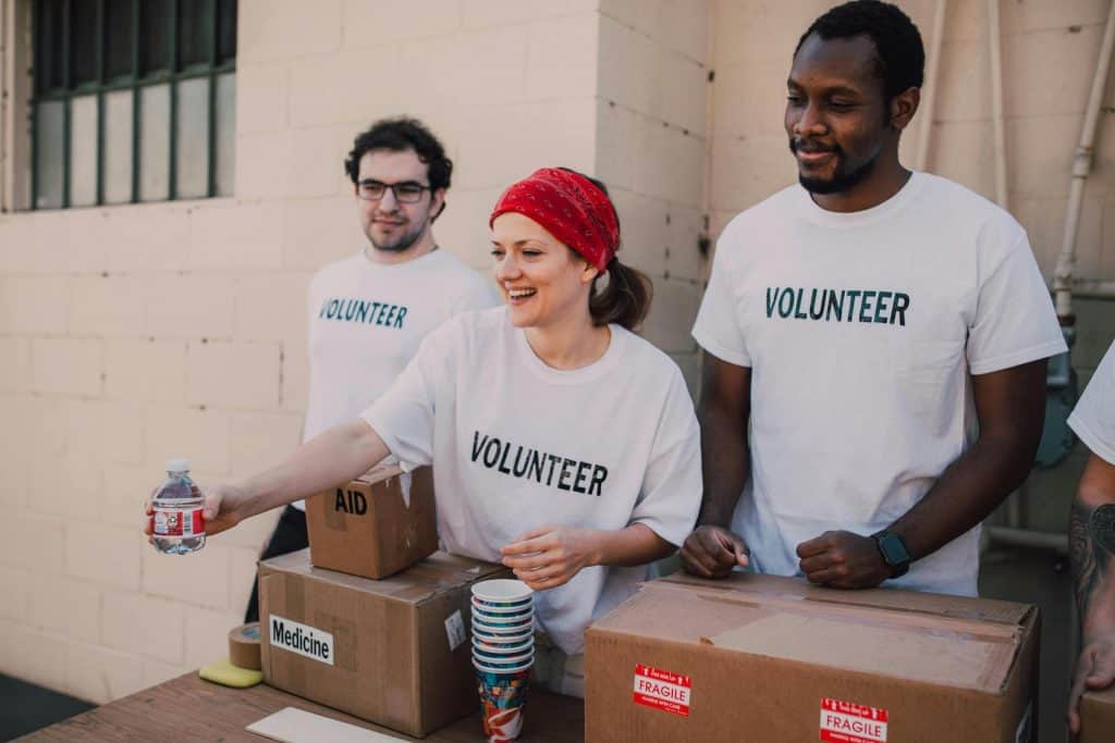 2 males and 1 female in volunteer shirts handing out small bottles of water. 