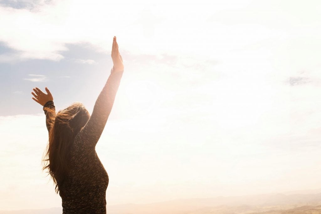 Woman holding her arms up in the air while looking at the sky. 