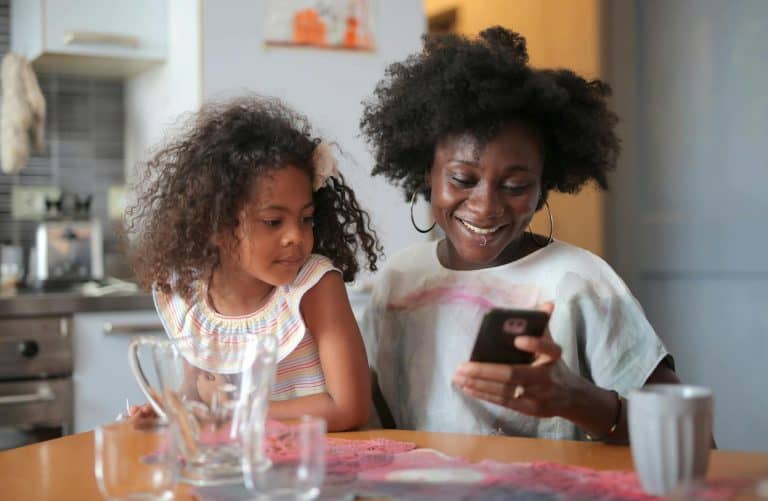 Mom and daughter looking down at a kid budgeting app on their phone whle smiling.