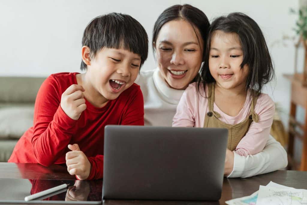 A mom with a positive money mindset looking at her computer with her 2 kids. They all look excited due to a small family financial win.