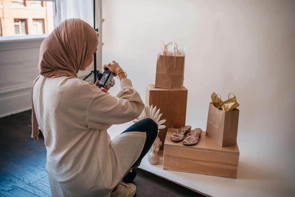 Shows a woman from behind who is taking a picture of a pair of sandals. 