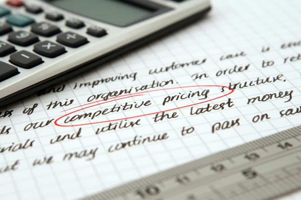 Writing on a piece of grid paper with the words "competitive pricing" circled in red. Also shows half of a calculator. 