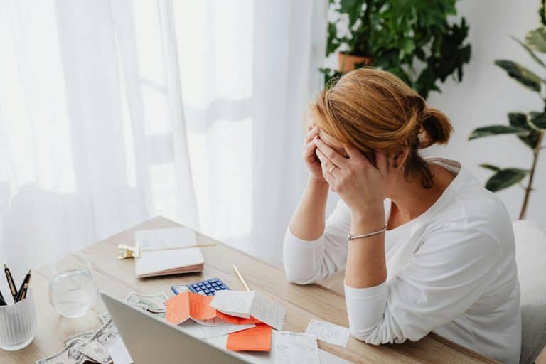 A woman sitting at her desk holding her head in her hands looking stressed.