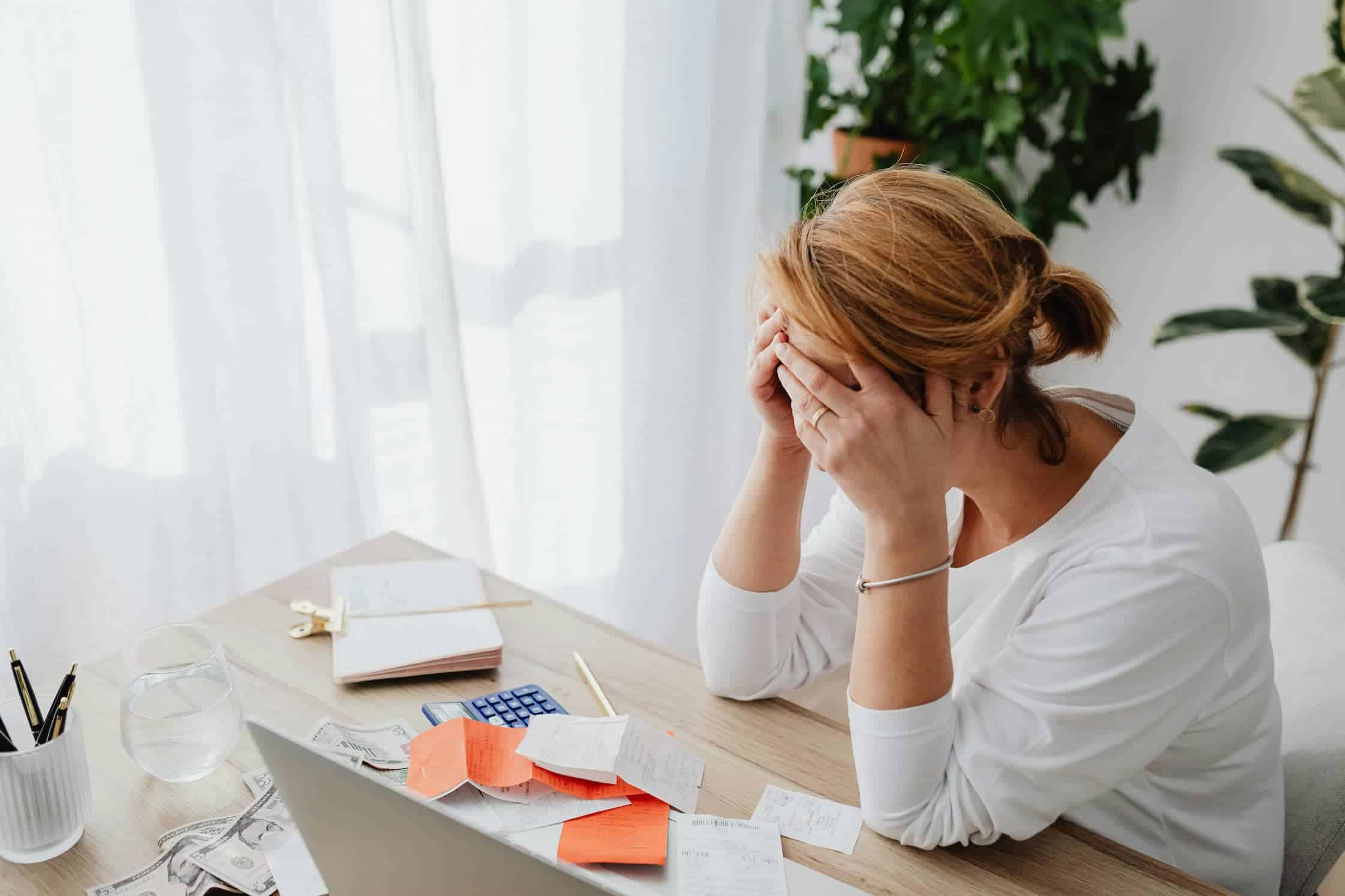 A woman sitting at her desk holding her head in her hands looking stressed.
