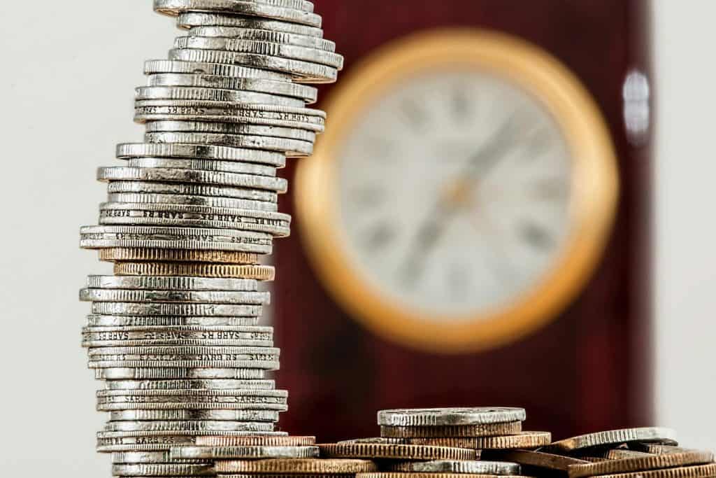 Image of a bunch of silver coins stacked up with a blurry image of a clock in the background.