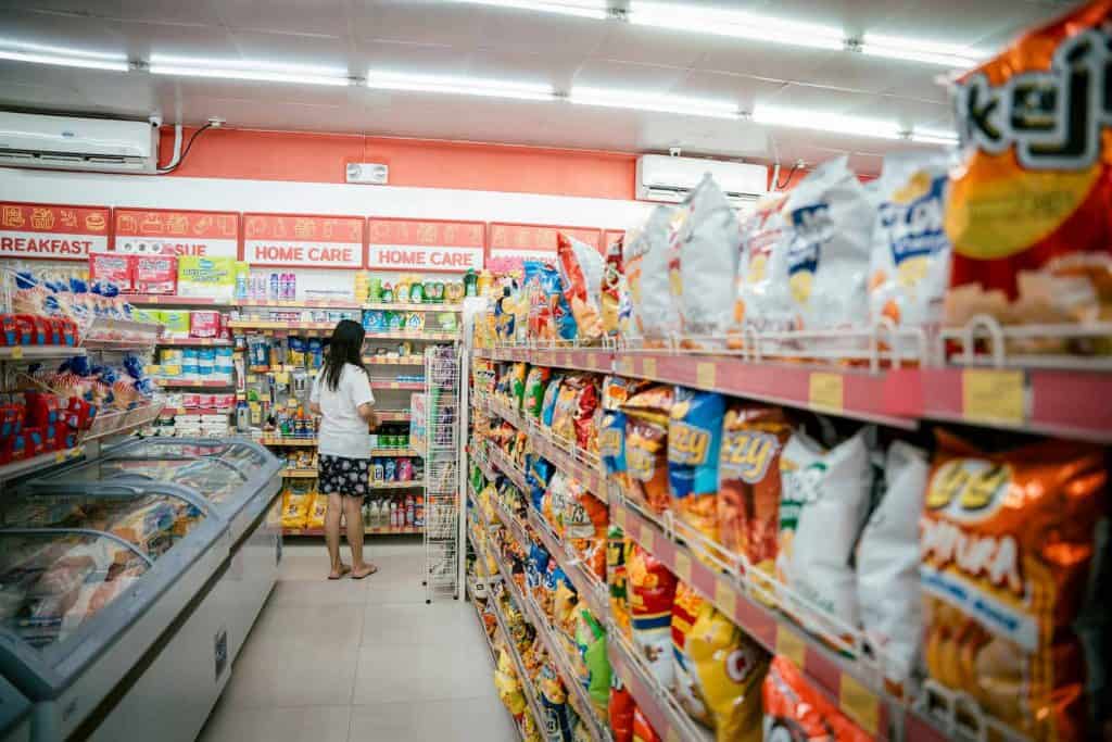 Image of a girl standing in grocery store surrounded by processed food such as chips. 