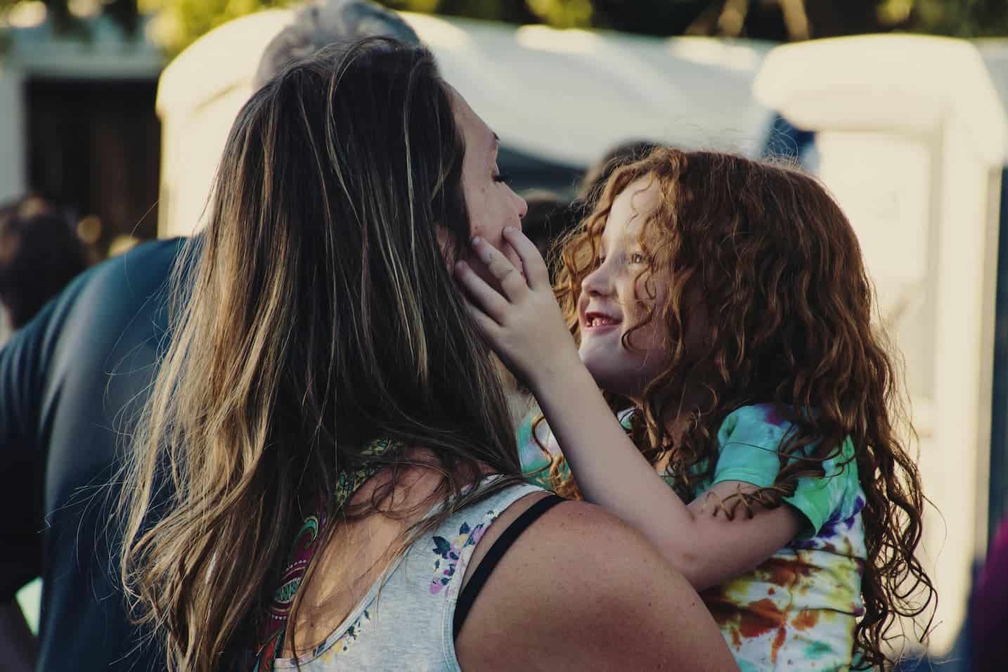 Single mom holding her daughter who is looking at her smiling.